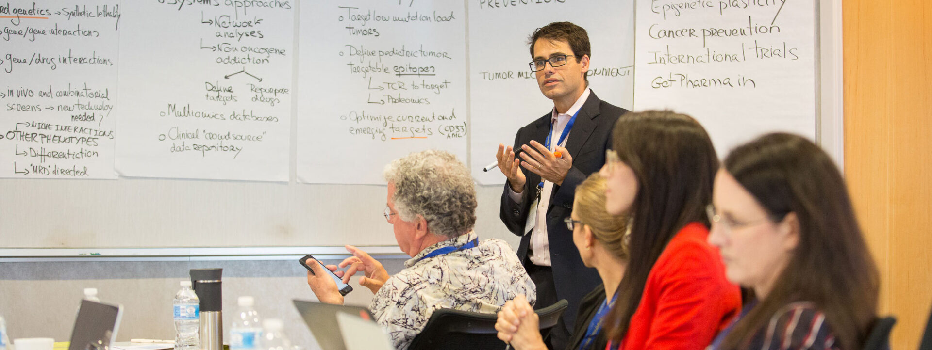 Man leading a workshop with four people in the foreground on their laptops