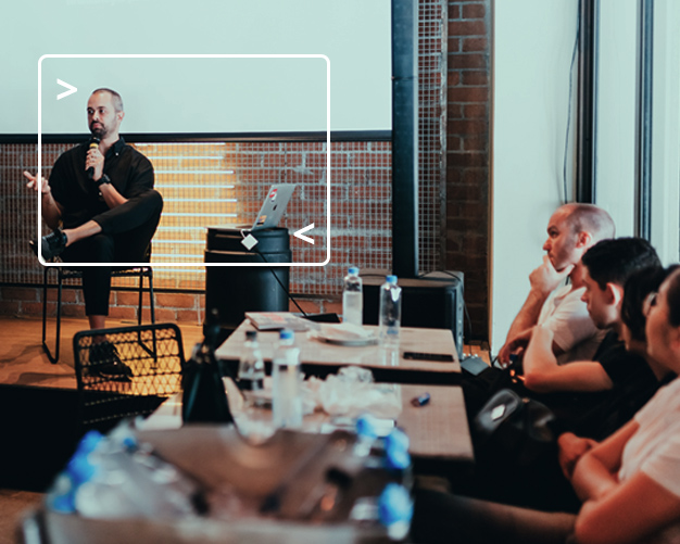 Man on stage with microphone speaking at event to small audience sitting at tables